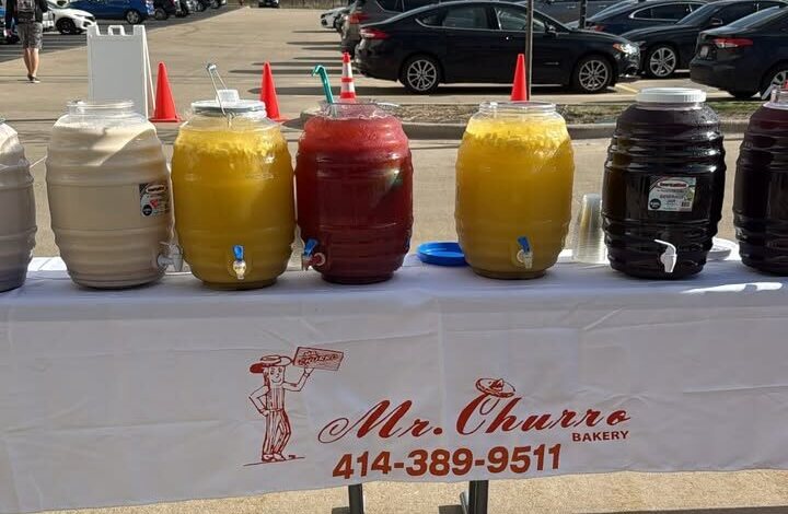 Mr. Churro catering setup: barrels of aguas frescas lined up on a table with the Mr. Churro branded tablecloth at an event.