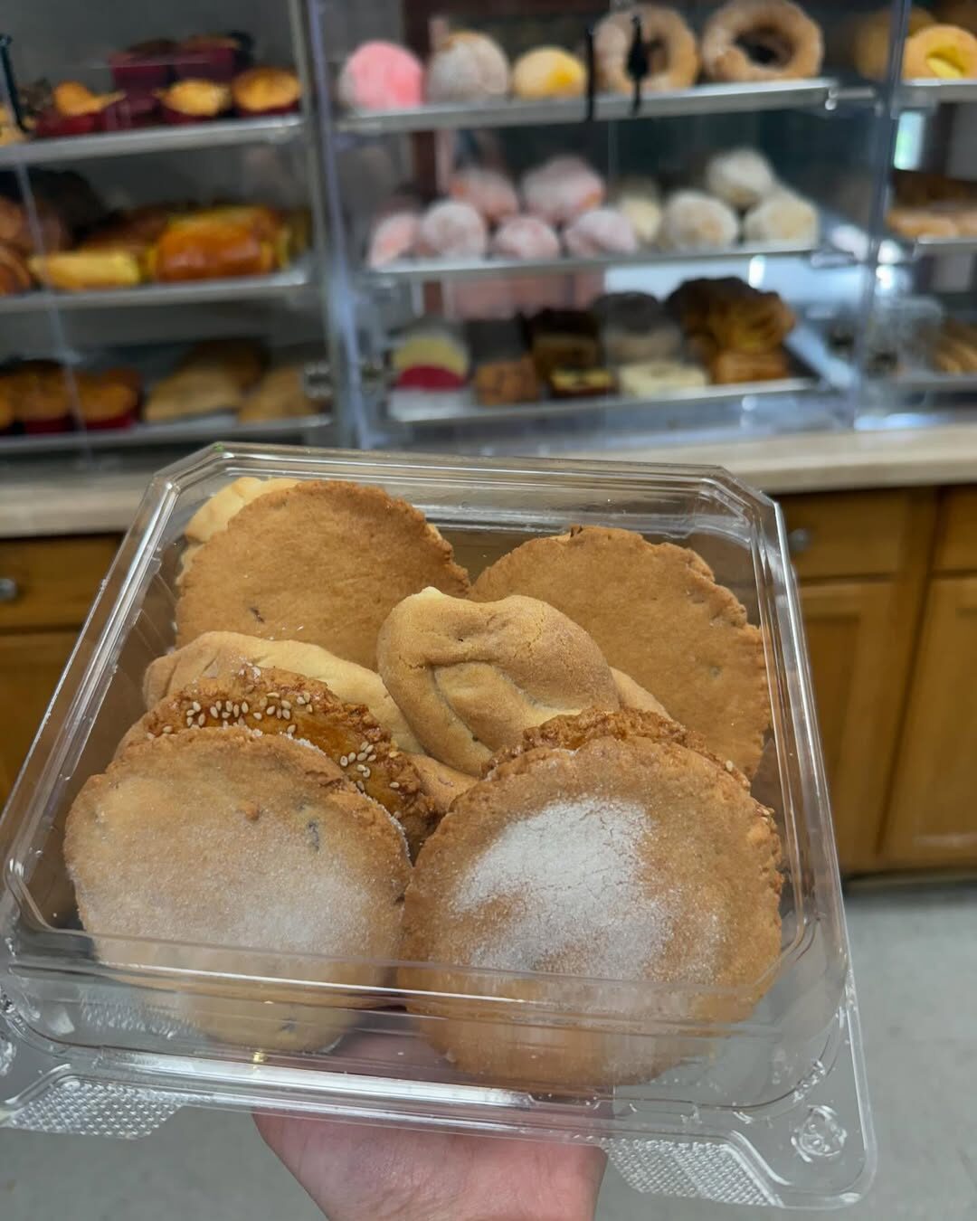 A box of freshly baked Mexican cookies and polvorones, with the full Mr. Churro bakery case and racks of pan dulce in the background.